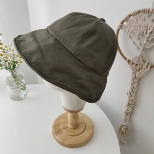 Detail of dark olive green sun hat on a display stand with minimalist floral decor