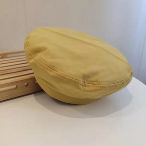 Close-up of yellow canvas beret hat showing fine stitching on wooden tray display