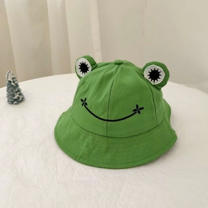 Detail eines grünen Frosch-Anglerhuts mit 3D-Augen und gesticktem Lächeln auf Baumwollstoff
