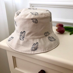 Detail view of beige cotton bucket hat with black butterfly print on a textured fabric