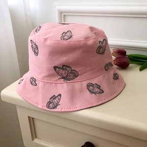 Pink canvas bucket hat with black butterfly prints on a white surface with tulips