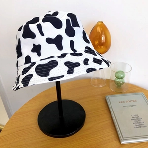 Détail d'un chapeau bob à motif vache sur support noir posé sur une table en bois