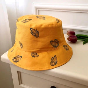 Close-up of yellow bucket hat featuring black hand-drawn butterfly prints and fine stitching