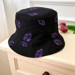 Close-up of black bucket hat featuring light purple butterfly patterns and canvas texture