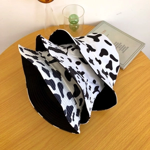 Trois bobs empilés avec motif vache noir et blanc sur une table en bois naturel