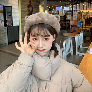 Close-up of cute plush brown beret with bear ears worn with a beige puffer jacket