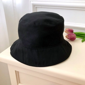 Top view of a black cotton bucket hat on wood with purple tulips and white wall