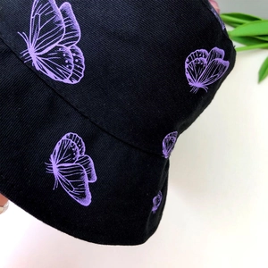 Close-up of black corduroy bucket hat with purple butterfly embroidery patterns