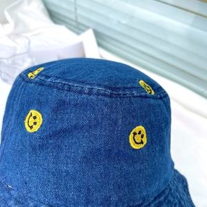 Macro detail of smiley face embroidery on dark blue denim bucket hat texture