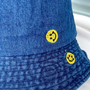 Close-up of indigo denim bucket hat featuring embroidered yellow smiley face and stitching