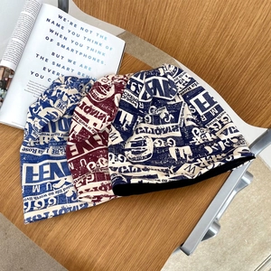Dettaglio di tre berretti in maglia blu, bordeaux e nero con stampa di giornale