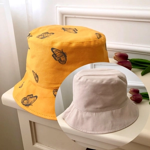 Detail of yellow canvas bucket hat with butterfly print and beige reversible option