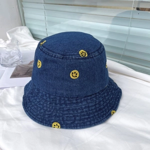 Detail of yellow smiley face embroidery on dark blue denim bucket hat texture