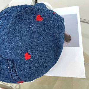 Detailed close-up of dark blue denim bucket hat with embroidered red heart patterns