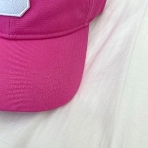 Detail of rose red baseball cap brim with multi-row stitching and white cloth embroidery