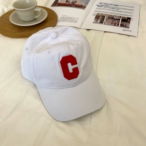 Close-up of white cotton baseball cap with red embroidered C letter on casual lifestyle background