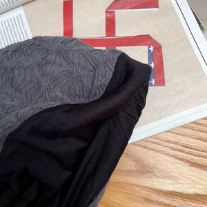 Detail der grauen Wellenstruktur und des schwarzen Stoffes einer weichen Beanie-Mütze