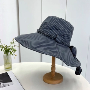 Detail of grey striped sun hat featuring a large bow and woven texture on a wooden stand