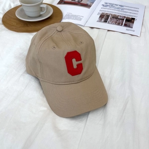 Detail shot of khaki cotton baseball cap with red embroidered C on a magazine