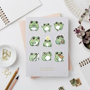 Flat-lay van groene cartoon kikkerstickers op ruitjespapier met briefpapier