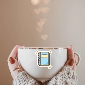 Autocollant carnet bleu sur mug en céramique blanche avec bord doré entre mains