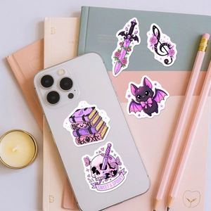 Detail of pink gothic stickers including skull and sword on white smartphone and journal