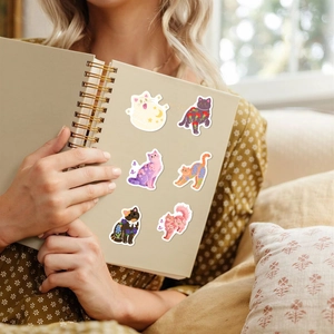 Artistic cat stickers with floral and celestial patterns on a spiral notebook cover