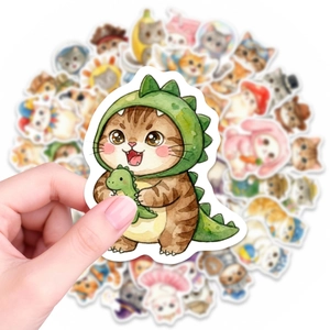 Gros plan d'une main tenant un autocollant de chat aquarelle en costume de dinosaure