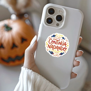 White phone case with blue fish sticker and Spanish text held in hand against pumpkins