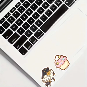 Nahaufnahme von niedlichen Cartoon-Cupcake- und Klavieraufklebern auf einem Laptop