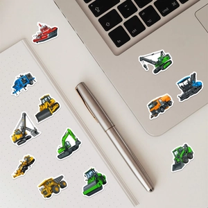 Detailed construction vehicle stickers scattered near laptop and dot grid notebook