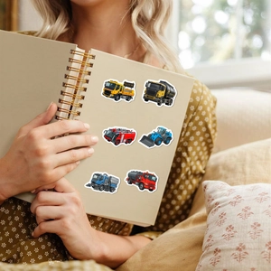 Cartoon construction vehicle stickers applied on a spiral notebook held by hands