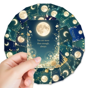 Detail of moon and flower affirmation cards with gold foil text being held by a hand