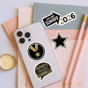 Detail of graduation stickers on a white smartphone and notebooks with gold and black accents