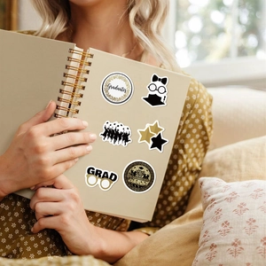 Close-up of black and gold graduation stickers on a spiral notebook in a lifestyle setting