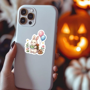 Cute bunny travel illustration on a white iPhone case held against a festive pumpkin background