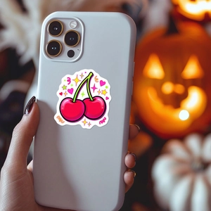 Detail of a cute cherry sticker with pink hearts on a white smartphone back