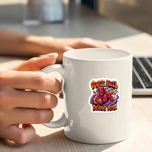Close-up of hand holding white ceramic Raise Hell devil mug on a bright wooden desk