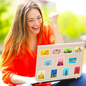 Flat illustration stickers of world landmarks on a silver laptop used outdoors by a woman