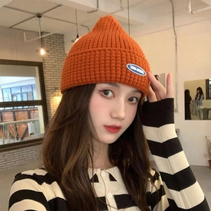 Detail of bright orange knitted beanie with textured wool weave and brand label on cuff