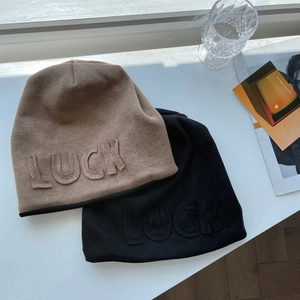 Detailed close-up of khaki and black knit beanies with textured LUCK embossed letters