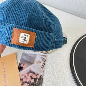 Detail of blue corduroy brimless docker hat featuring leather patch and metal strap buckle