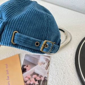 Close-up of blue corduroy docker hat featuring adjustable bronze metal buckle strap