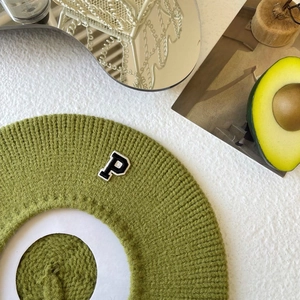 Detail of green chunky knit beret showing textured wool pattern and embroidered letter P