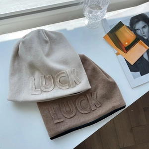 Detail of LUCK letter patch embroidery on soft ribbed knit beanies in beige and light brown