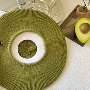 Detail view of avocado green knit beret cap on a rustic table with decorative props
