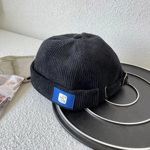Detail of black corduroy docker hat with blue logo tag and vintage metal buckle adjustment