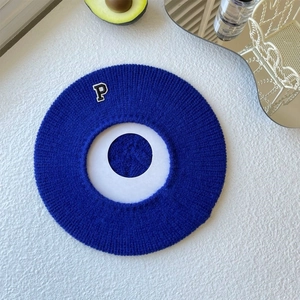 Flat lay of royal blue knit beret with letter P patch on textured white background