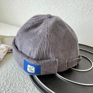 Detail of gray corduroy docker hat showing adjustable metal buckle and blue textile label
