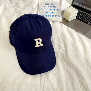 Detailed embroidery of white letter R on navy blue cotton baseball cap in lifestyle setting